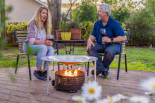 Load image into Gallery viewer, A couple sitting near a fire pit that has a HeatSaver heat deflector
